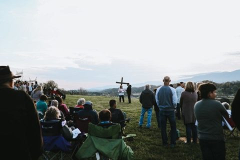 large group of people gather on top of mountain overlooking a cross and the horizon for a sunrise worship service
