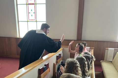 A minister high fives a group of kids sitting in a pew