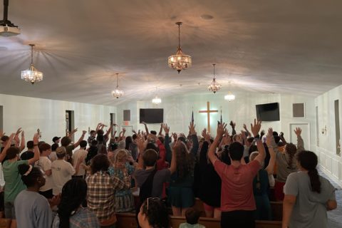 Unicoi Christian Church, a large group of teenagers worship together, lifting up their hands.