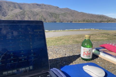 A computer screen on a blanket with a Dr. Enuf drink beside it and Lake and Mountains in the background.