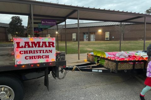 Sign that reads Lamar Christian Church connected to a trailer for a float in a parade. School in the background