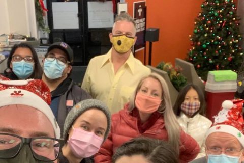 Group of people wearing masks but gathered around a Christmas tree