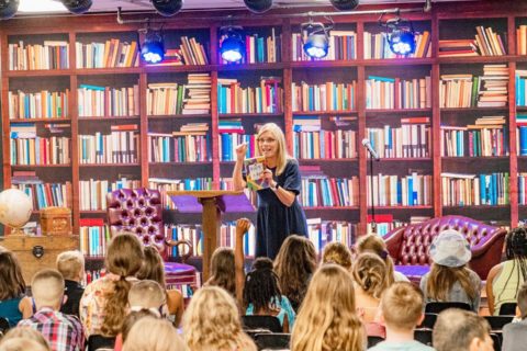 New Hope Christian Church - Woman with blond hair teaches children with a wall of books behind her