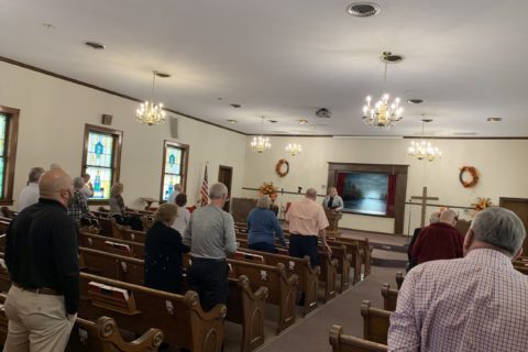 a group of adults worship in a small sanctuary.