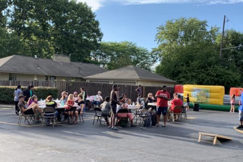 people gather around picnic tables in a church parking lot