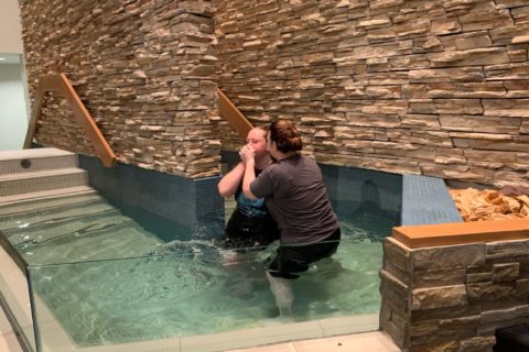 a woman baptizes a young woman in a church baptistry