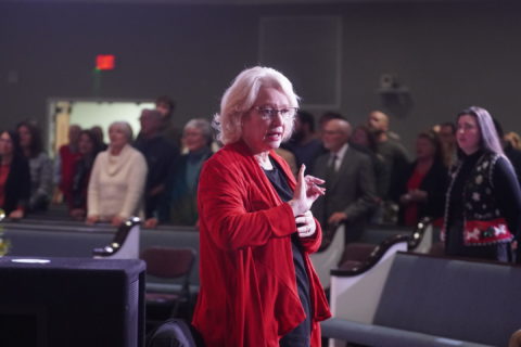 A woman wearing a red sweater talks to a crowd at Boones Creek Christian Church