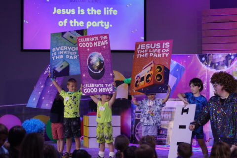 Four kids shout with signs on stage that read 