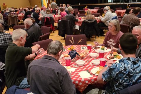 Crossroads KS Christian Church: large group of people sit around tables with checkered cloth in a large fellowship hall. They are eating BQ.