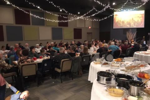 Newton Christian Church - a banquet inside with lights hanging down a people sit in long table rows with a screen in front