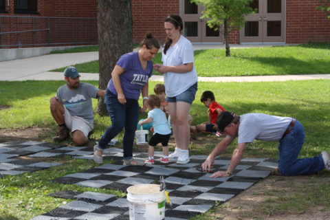 Kids set up a life size checkers board on a green lawn