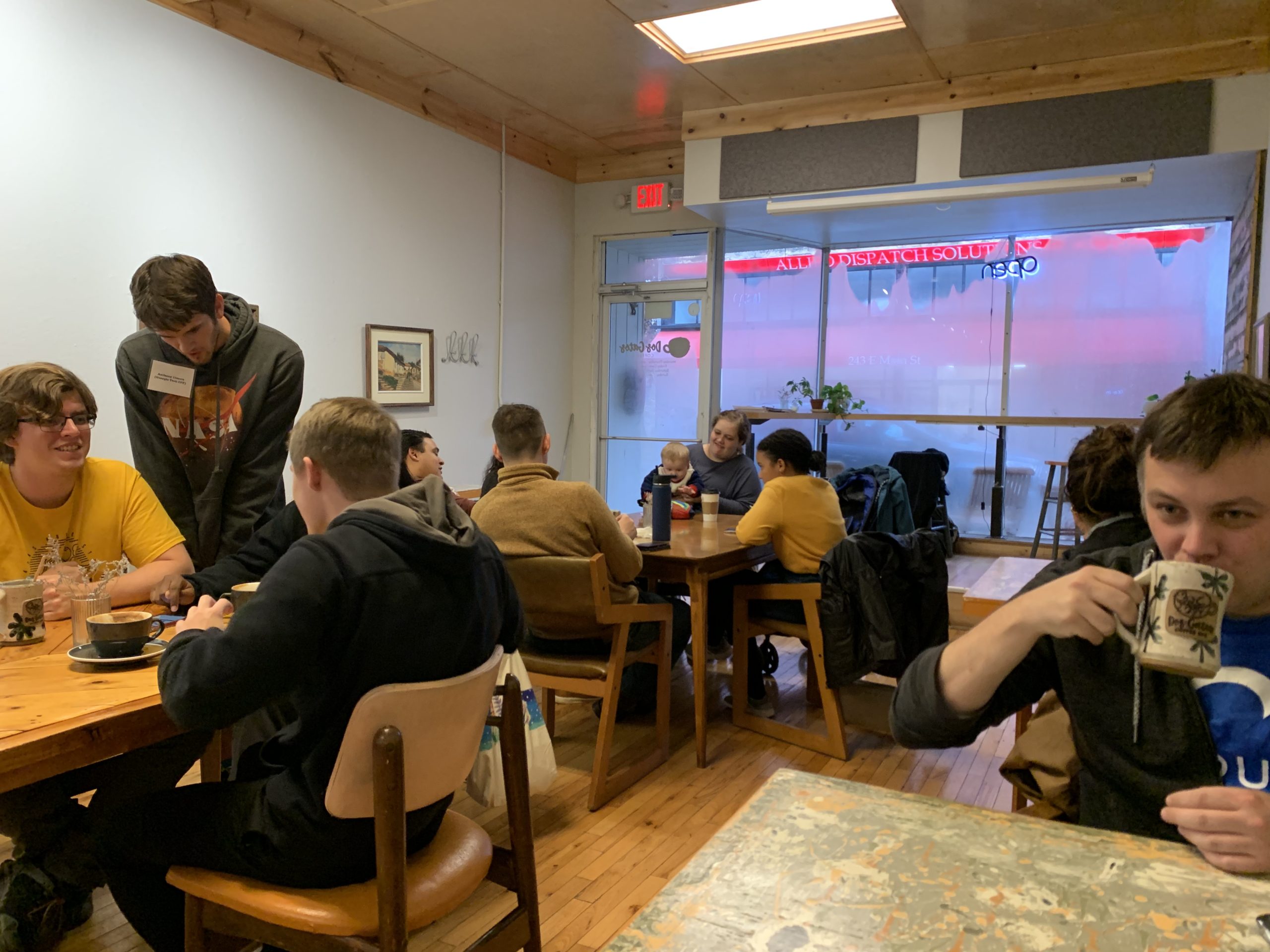 Young group hanging out in a cafe. A young man sips his coffee drink in front right corner