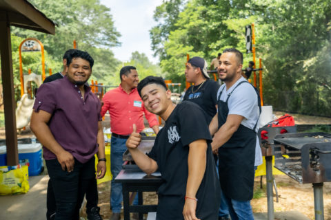 Latino youth gather at a grill out. The center boy up front is giving a thumbs up.