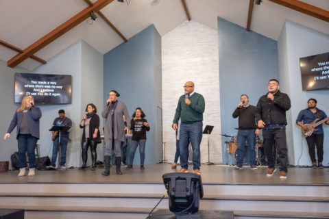 A large group of POC Worship singers perform on a stage at a church.